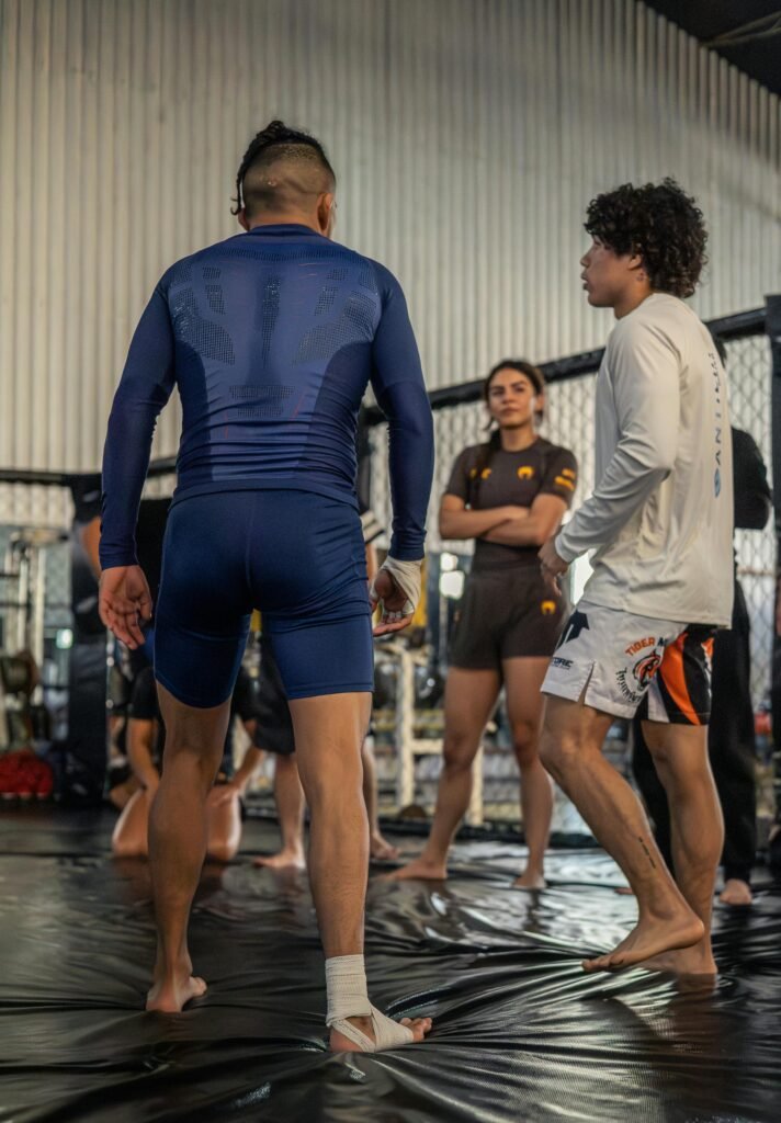 Martial arts training session with three adults in a gym setting, focused on mixed martial arts practice.
